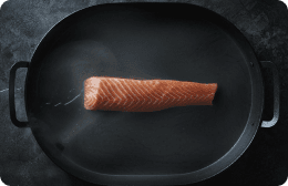 Een stuk zalm dat in een hete pan ligt te bakken